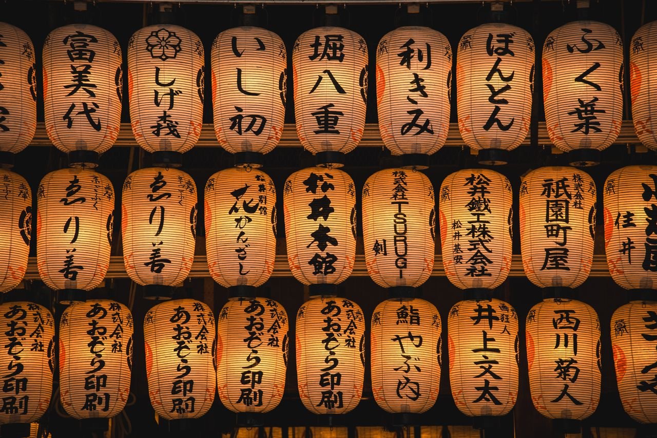 A display of glowing Japanese paper lanterns with kanji characters set against a dark background.